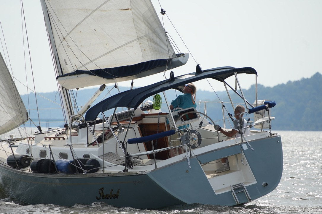 People aboard a sailboat with white sails and a blue canopy, viewed from the stern.
